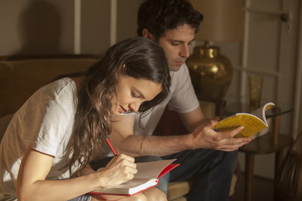Carla (Katie Holmes) writes in her diary as Marco (Luke Kirby) reads her poety book
