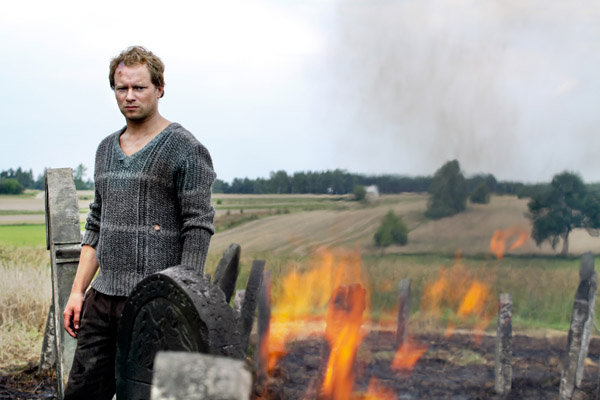 Jozek (Maciej Stuhr) stands by gravestones in a burning field